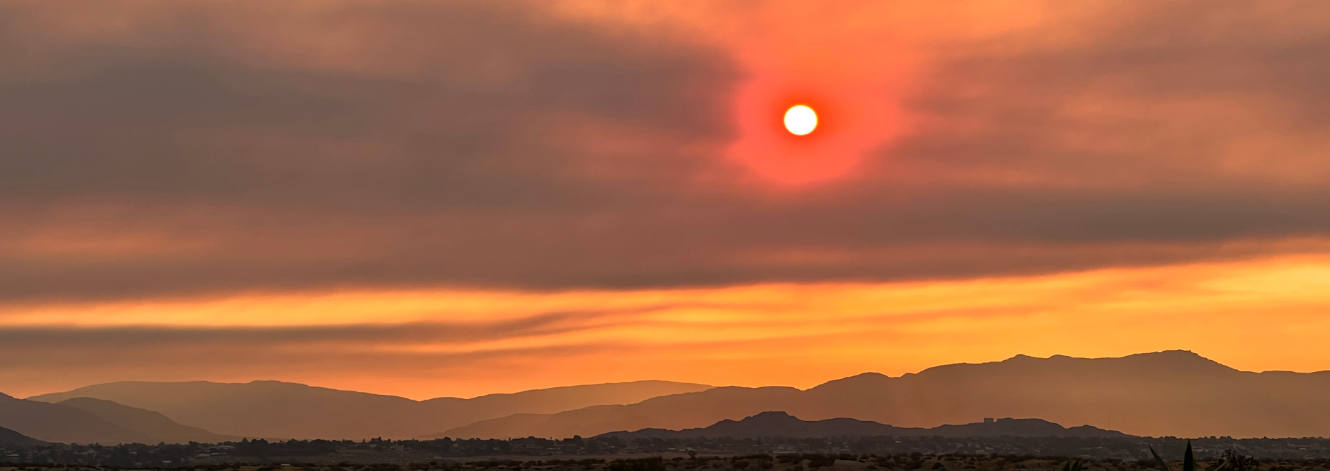 Sun appears red as it peeks through heavy wildfire smoke clouds.